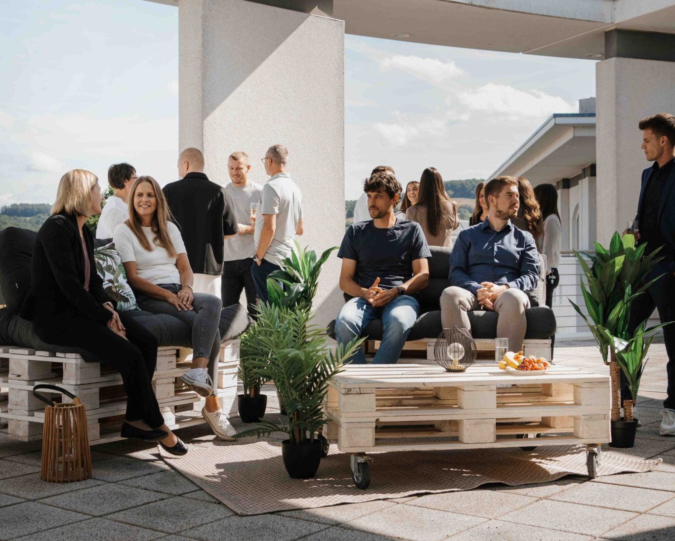Personen unterhalten sich in einer modernen, offenen Lounge mit Palettenmöbeln, Team am Standort Großwallstadt (Kreis Miltenberg)