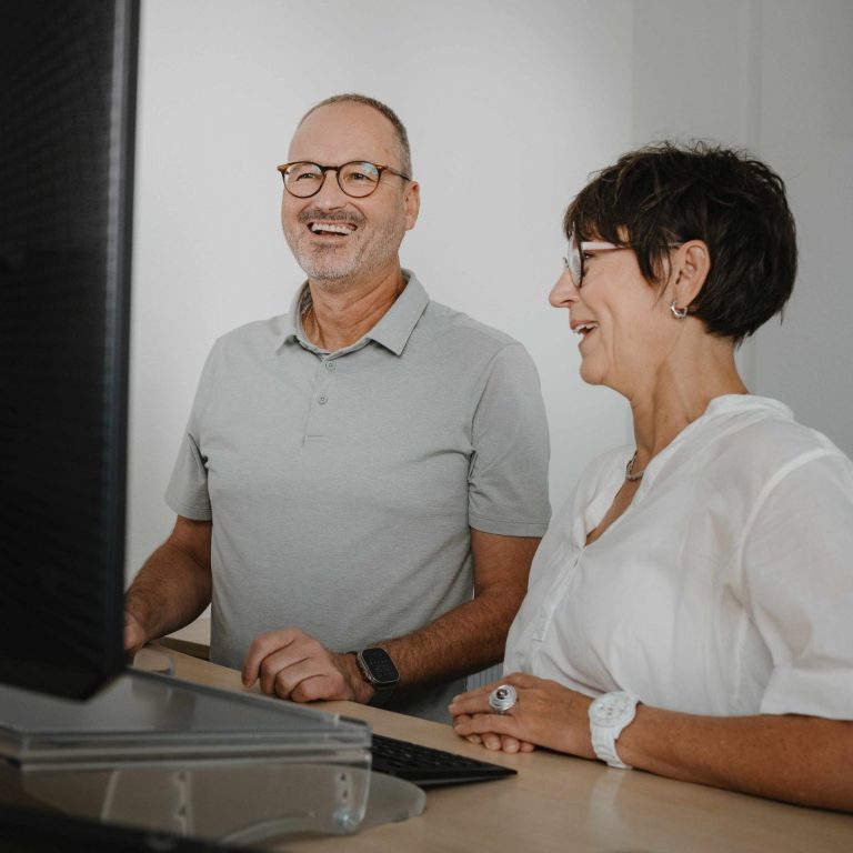 Ein Mann und eine Frau lächeln beim Blick auf einen Computerbildschirm in den Kanzleiräumen in Großwallstadt (Raum Aschaffenburg)