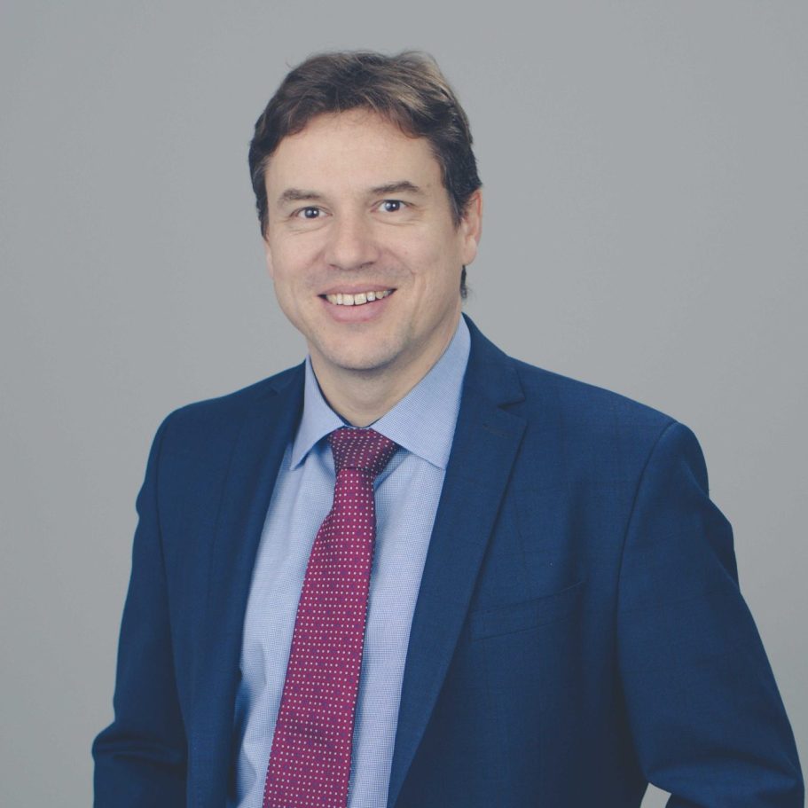 Mann in Anzug mit Krawatte lächelt vor grauem Hintergrund. Frank Wolf, Steuerberater, Geschäftsführer