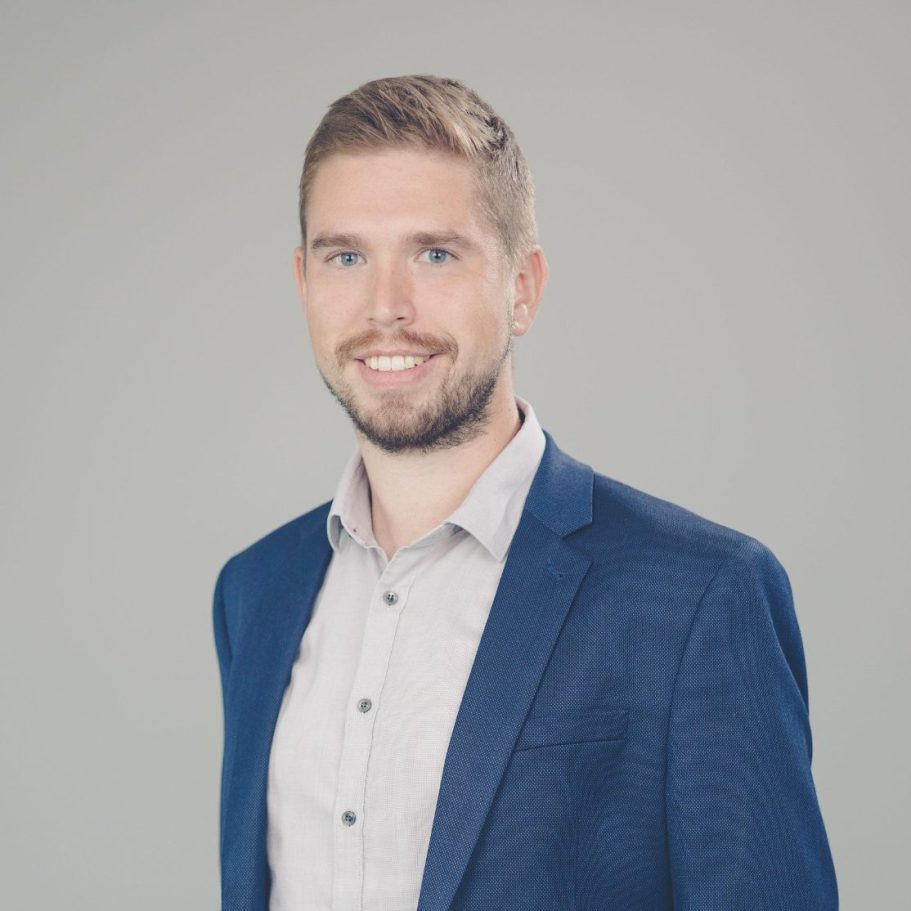 Ein lächelnder Mann in einem blauen Anzug und einem hellen Hemd vor neutralem Hintergrund. Timo Wolz, Steuerberater, Geschäftsführer